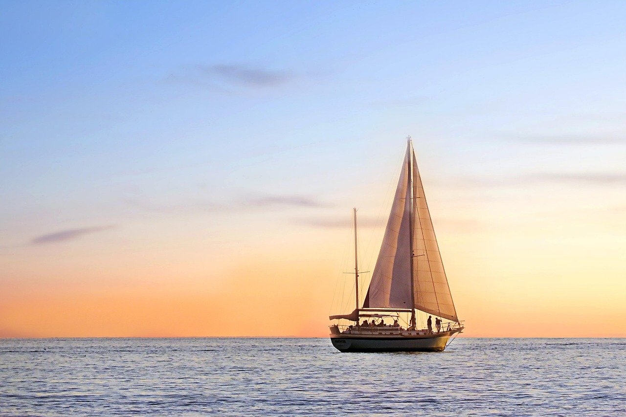 a sail boat floats on blue water with an orange sunset background